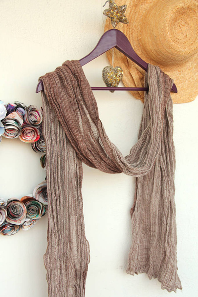a soft light brown cotton scarf on a purple coat hanger with a golden heart and a star straw hat and wreath - Photo, Image