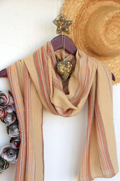 Een zachte beyge katoenen sjaal op een paarse kapstok met een gouden hart en een ster strooien hoed en krans - Foto, afbeelding