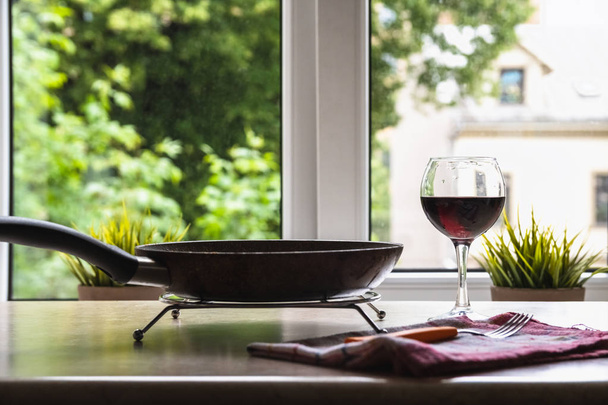 Patelnia teflonowa i kieliszek wina na stole przeciwko okna - Zdjęcie, obraz