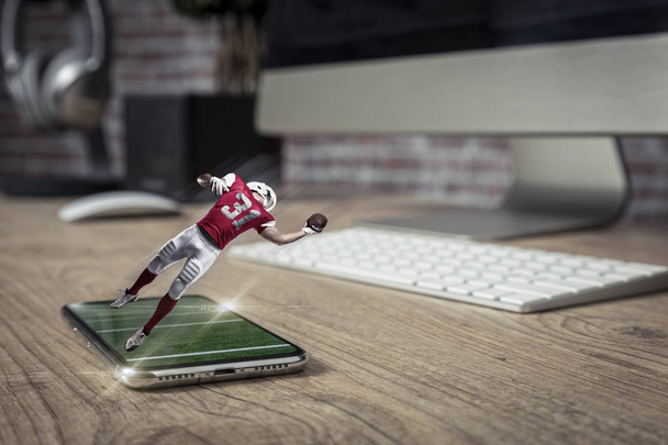 Labdarúgó játékos-val egy piros egységes játék, és jön ki a teljes képernyő telefon, egy fából készült asztal. Néz egy focimeccsen a követelés fogalmát. másol hely. - Fotó, kép