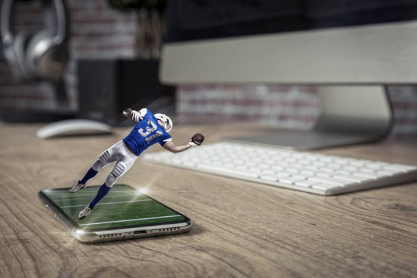 Football Player with a blue uniform playing and coming out of a full screen phone on a wooden table. Watching a football game on demand concept. copy space. - Valokuva, kuva