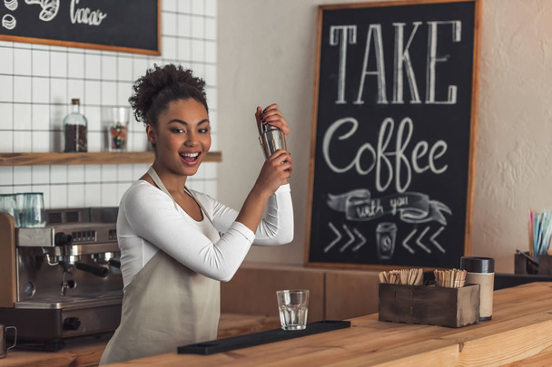 Szép Afro-amerikai barista kötény készül egy koktél shaker és mosolyogva állva a inspirációk - Fotó, kép