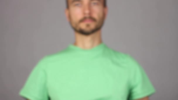 ernster Mann in grünem Hemd hebt vor ihm auf der rechten ausgestreckten Hand ein neues Kondom, Porträt des Mannes verschwommen - nicht im Fokus, Konzept von gesundem Lebensstil und Geburtenkontrolle, grauer Hintergrund   - Filmmaterial, Video