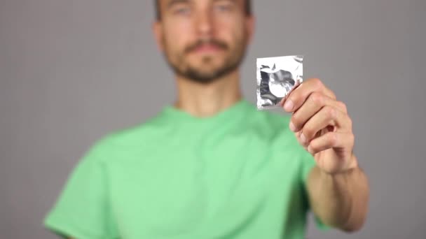 muž v zeleném tričku vyvolává mu na jeho levou nataženou ruku nový kondom, pravá ruka dělá gesto palec nahoru, radosti a očekávání rozkoše, správný postoj k ochraně, šedé pozadí  - Záběry, video