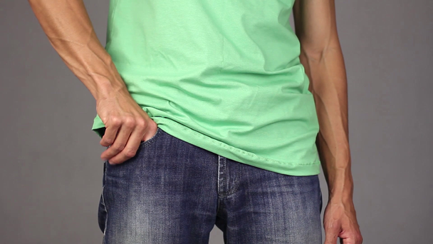 man in green shirt takes out new condom from the front pocket of blue jeans, concept of relationships based on trust and responsibility, gray background - Footage, Video