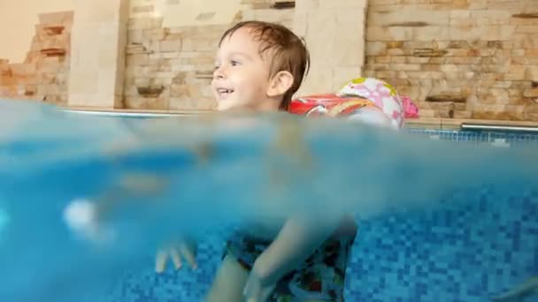 Vídeo 4k do menino sorrindo feliz da criança no anel inflável que nada na piscina interna no hotel
 - Filmagem, Vídeo