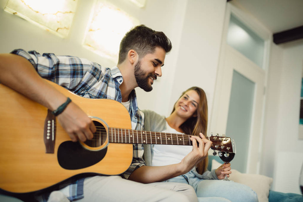 Portret van vriendje met zijn vriendin binnenshuis te genieten en gitaar spelen - Foto, afbeelding
