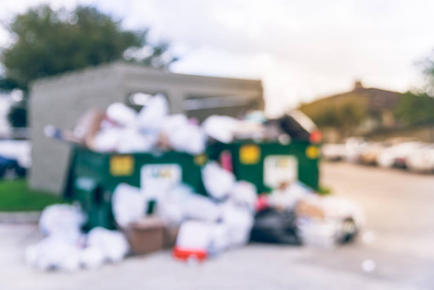 verwischte einen überquellenden Müllcontainer im Bauhof eines Mehrfamilienhauses in Demut, Texas, us. Überfüllt und auf dem Boden voller Hausmüll, Plastiktüten, Matratzen, Kartons nach den Feiertagen. Abfallwirtschaft in der Stadt - Foto, Bild