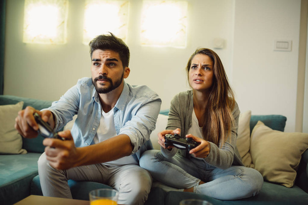 Портрет молодой пары, играющей в видеоигры, сидящей дома на диване
 - Фото, изображение