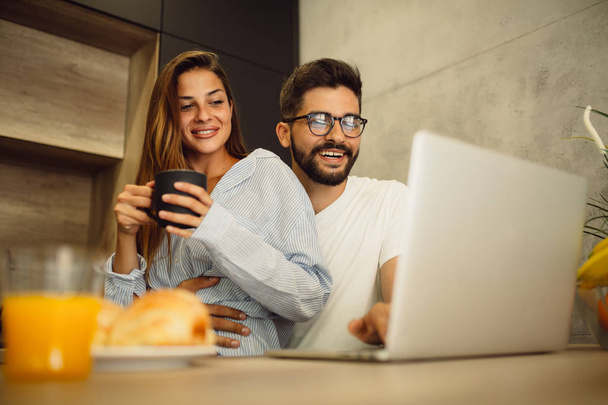 Retrato de pareja joven que se divierte mientras lee noticias en el portátil y bebe café de la mañana
 - Foto, Imagen