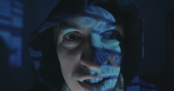 Close up of Crazy hacker programmer in hood with binary code reflection on his face in dark room at night. Portrait of dangerous Mad man programmer. - Footage, Video
