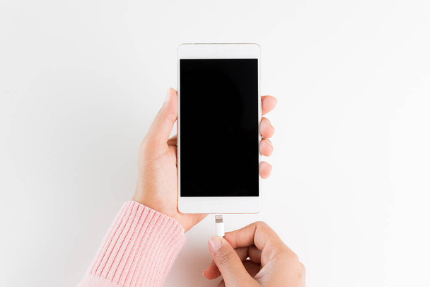 Woman hands connecting charger to smartphone on white table background. - Zdjęcie, obraz