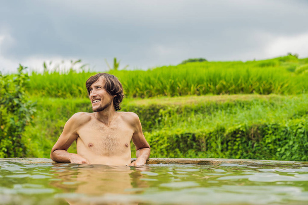 man tourist posing in Belulang Hot Spring pool with rice field on background, Bali, Indonesia - Фото, изображение