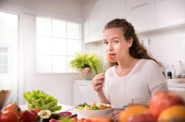 Mujer joven sana comiendo ensalada en la cocina
 - Foto, imagen