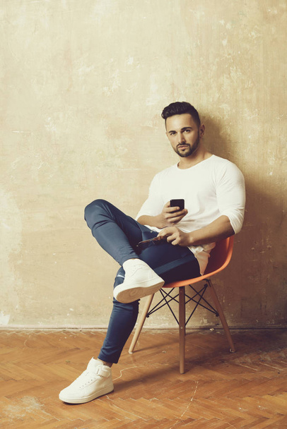 man or sexy macho sitting on chair with smartphone - Фото, изображение