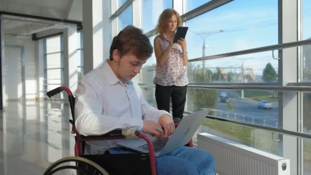 инвалид бизнесмен на инвалидной коляске у окна с ноутбуком рядом женщина использует планшет 4k
 - Кадры, видео