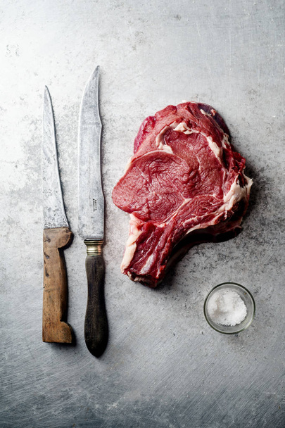 Raw beef steak with knifes and pinch of salt on metallic background - 写真・画像