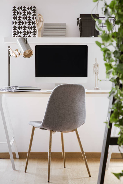 Grey chair at desk with desktop computer and lamp in modern white workspace interior. Real photo - Foto, imagen