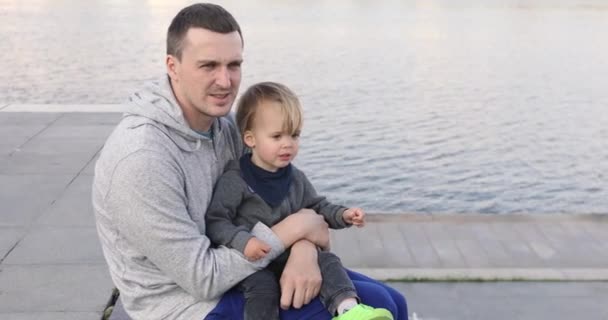 Νεαρός άνδρας κάθεται στο pier με μωρό - Πλάνα, βίντεο