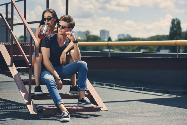 Sex tussen verschillendre rassen paar met fles rum zittend op de trap op dak - Foto, afbeelding
