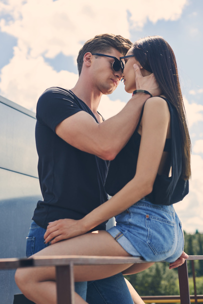 multiethnic hot couple going to kiss while sitting on railings on roof - Foto, Bild