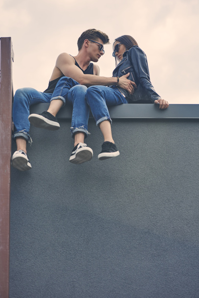 bottom view of stylish interracial couple flirting and hugging on roof - Φωτογραφία, εικόνα
