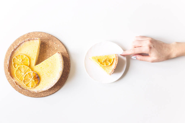 Лимонный пирог с сушеными лимонами в качестве украшения и порезанным кусочком в женских руках. На белом фоне. Вид сверху, плоский. Домашняя минимальная поддержка
 - Фото, изображение