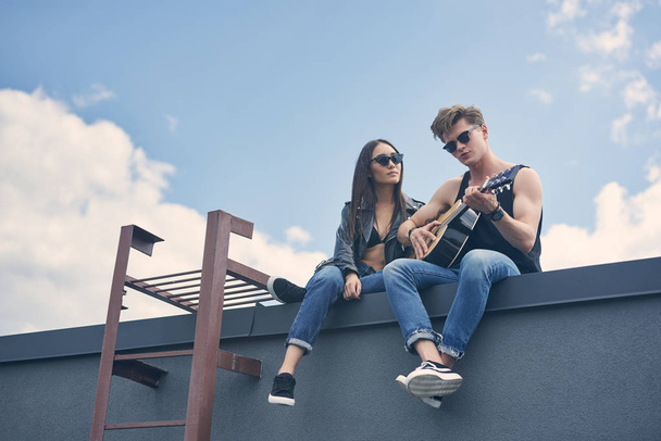 屋根の上の彼のアジアのガール フレンドのアコースティック ギターで遊んでハンサムな彼氏 - 写真・画像