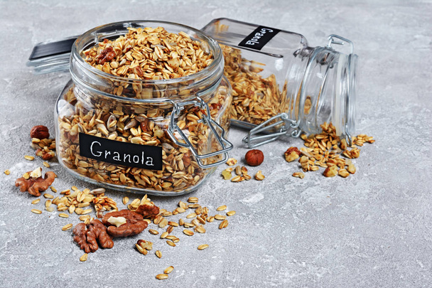 Healthy breakfast homemade granola with nuts and sunflower seeds in open glass jars on gray concrete background - Foto, imagen
