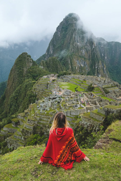 A girl in a red poncho sits and stares at Machu Pakchu Peru January, 2018 - Фото, зображення