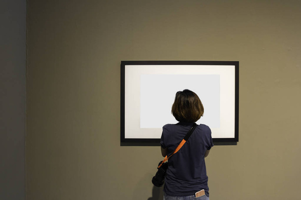 Frau betrachtet leeren Fotorahmen an Wand in Kunstgalerie. - Foto, Bild