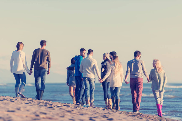 Bir grup genç arkadaş, güz günü boyunca kumsalda birlikte koşuyorlar. - Fotoğraf, Görsel