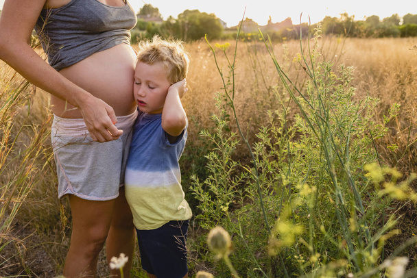 Child embraced his pregnant mother at sunset. - Photo, Image