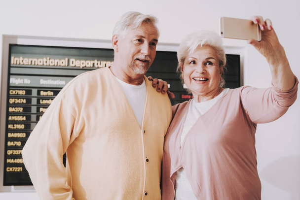 Old Couple Taking Photo in Airport in Waiting Room. Senior Person in Airport. Tourism Concept. Couple in Voyage. Airport Terminal. Vacation for Pensioner. People with Baggage. Travelers on Vacation. - Photo, image