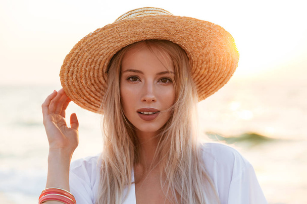 Image of beautiful cute blonde woman wearing hat outdoors at the beach looking camera. - Foto, afbeelding