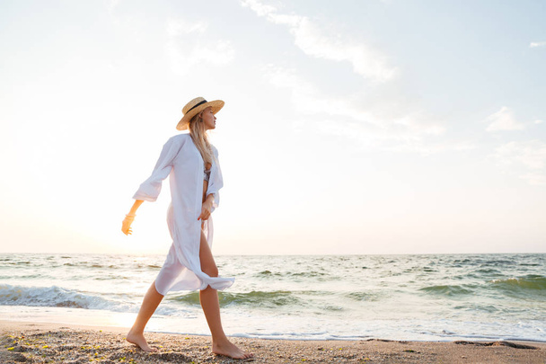 Picture of beautiful young blonde woman with hat walking outdoors at the beach. - Foto, imagen
