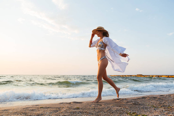 Foto de una bonita joven con sombrero caminando al aire libre en la playa
. - Foto, Imagen