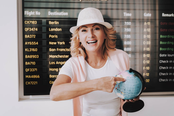 Woman in Cap with Globe in Airport in Waiting Room. Senior Person in Airport. Tourism Concept. Woman in Voyage. Airport Terminal. Vacation for Pensioner. Person with Baggage. Traveler on Vacation. - Foto, Bild