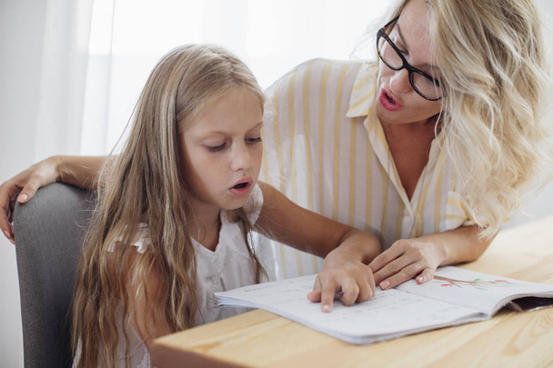 Cute Caucasian girl learning to read with her beautiful mother helping. - Foto, Bild