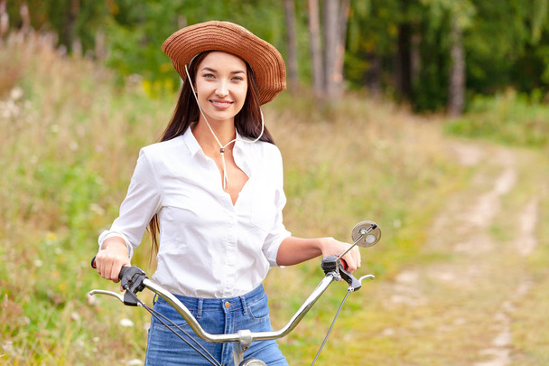 Mulher com uma bicicleta preta em um parque de verão ou floresta
 - Foto, Imagem