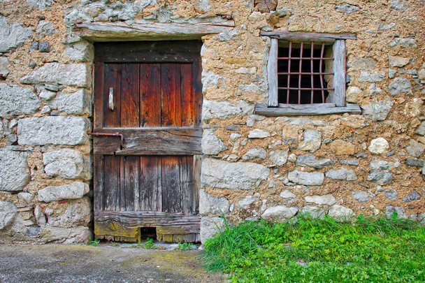 Αρχαία ξύλινη πόρτα με κάγκελα παραθύρων στο σπίτι του βότσαλα των αρχαίων συνόρων. - Φωτογραφία, εικόνα
