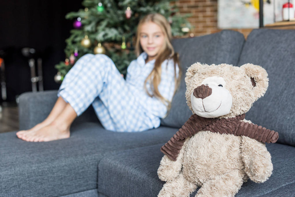 close-up view of teddy bear and child in pajamas sitting on couch behind at christmas time - Фото, изображение
