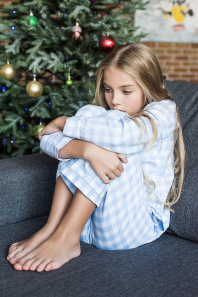 gyerek pizsama ül a kanapén karácsonykor ideges  - Fotó, kép