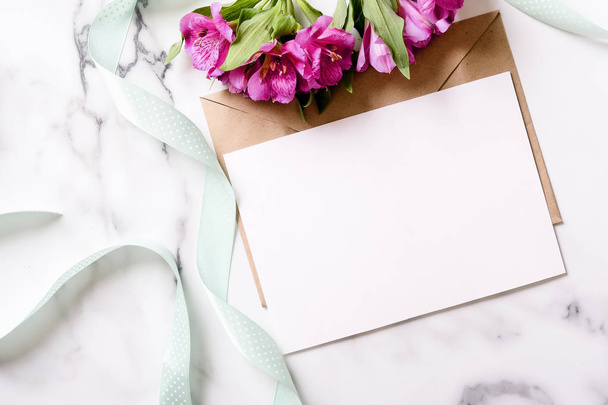 Marble desk with pink flowers, postcard, kraft envelope, twine, cotton branch, invitation card with copy space for your text. Flat lay, top view. Woman's day or mother's day mockup. - Foto, immagini