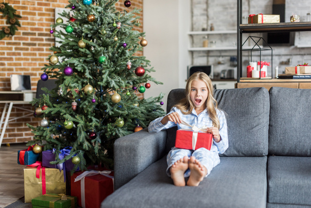 enfant surpris en pyjama ouvrant cadeau de Noël et regardant la caméra
  - Photo, image