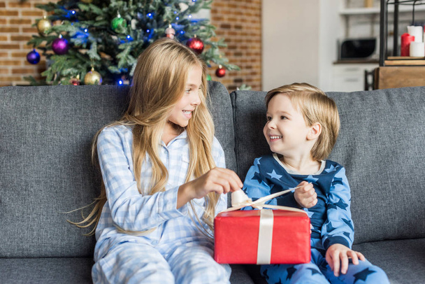 cute happy kids in pajamas holding christmas present and smiling each other - Foto, Imagen
