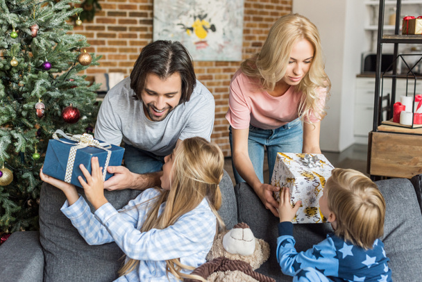 padres presentando regalos de Navidad a niños felices en pijama
 - Foto, imagen