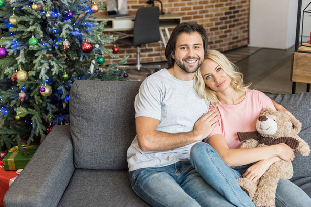 μεγάλη γωνία προβολής του όμορφη happy νεαρό ζευγάρι κάθεται στον καναπέ και να χαμογελά στη φωτογραφική μηχανή στο χρόνο Χριστουγέννων - Φωτογραφία, εικόνα