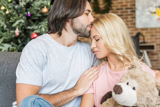 handsome young man kissing beautiful girlfriend with teddy bear at christmas time - Foto, Bild