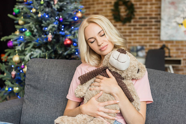 beautiful young woman with closed eyes hugging teddy bear at christmas time - Fotó, kép